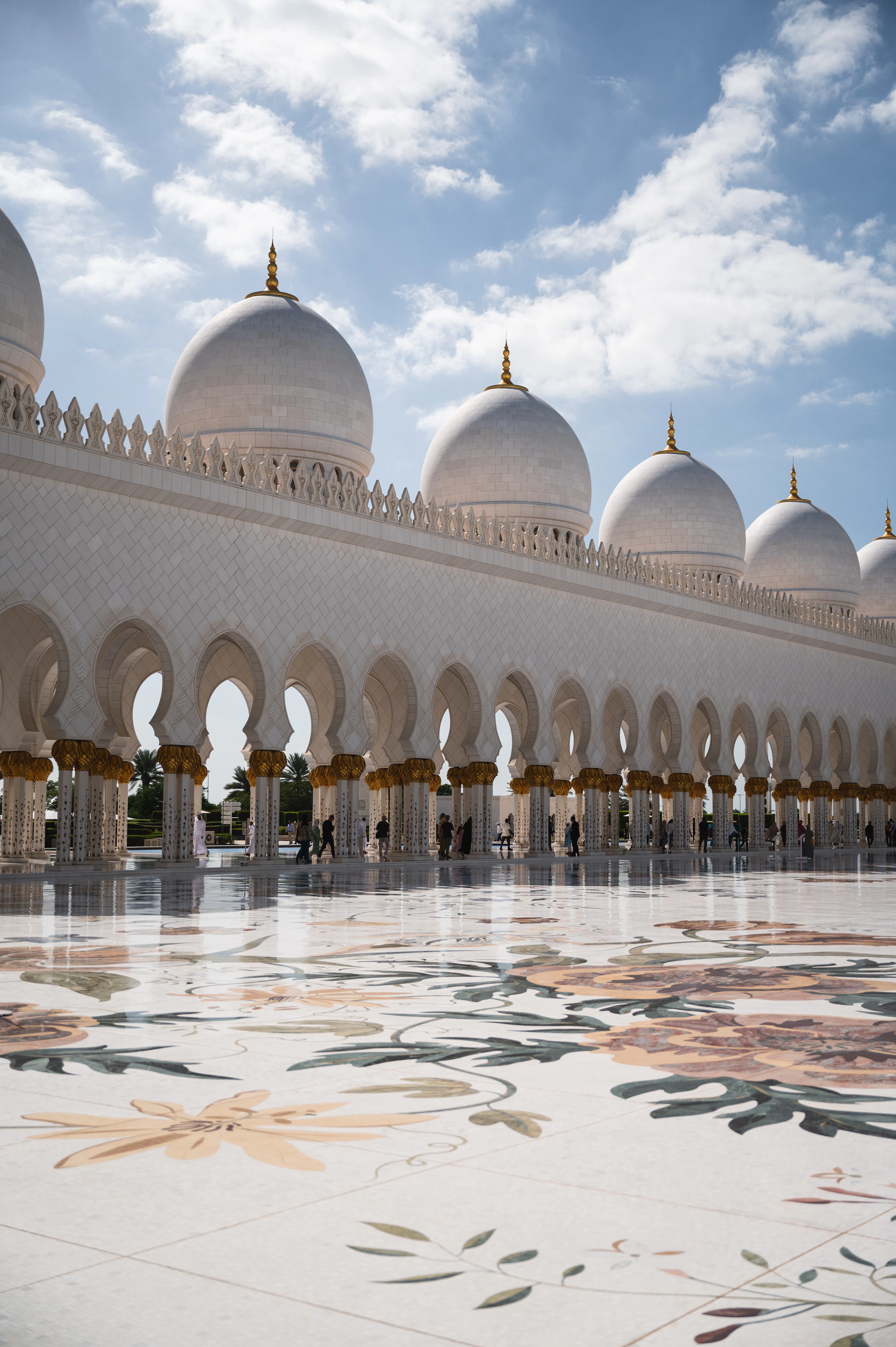Domes and gold finials of Sheikh Zayed Grand Mosque rise beneath a sky full of white clouds.