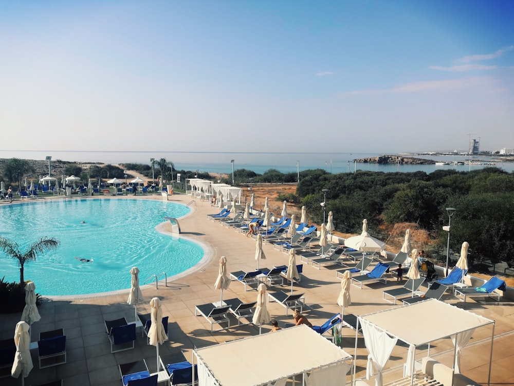 a large swimming pool surrounded by lawn chairs and umbrellas