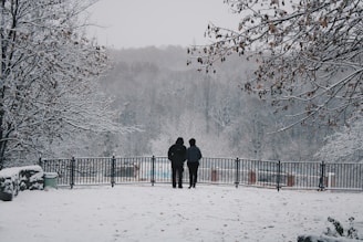 two people standing in the snow near a fence