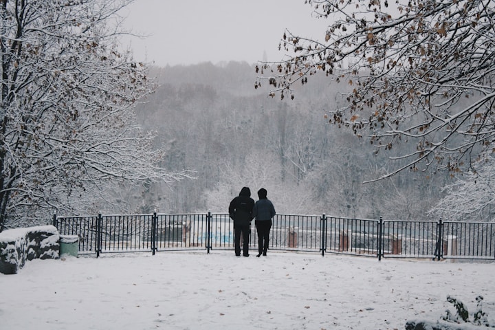 two people standing in the snow near a fence