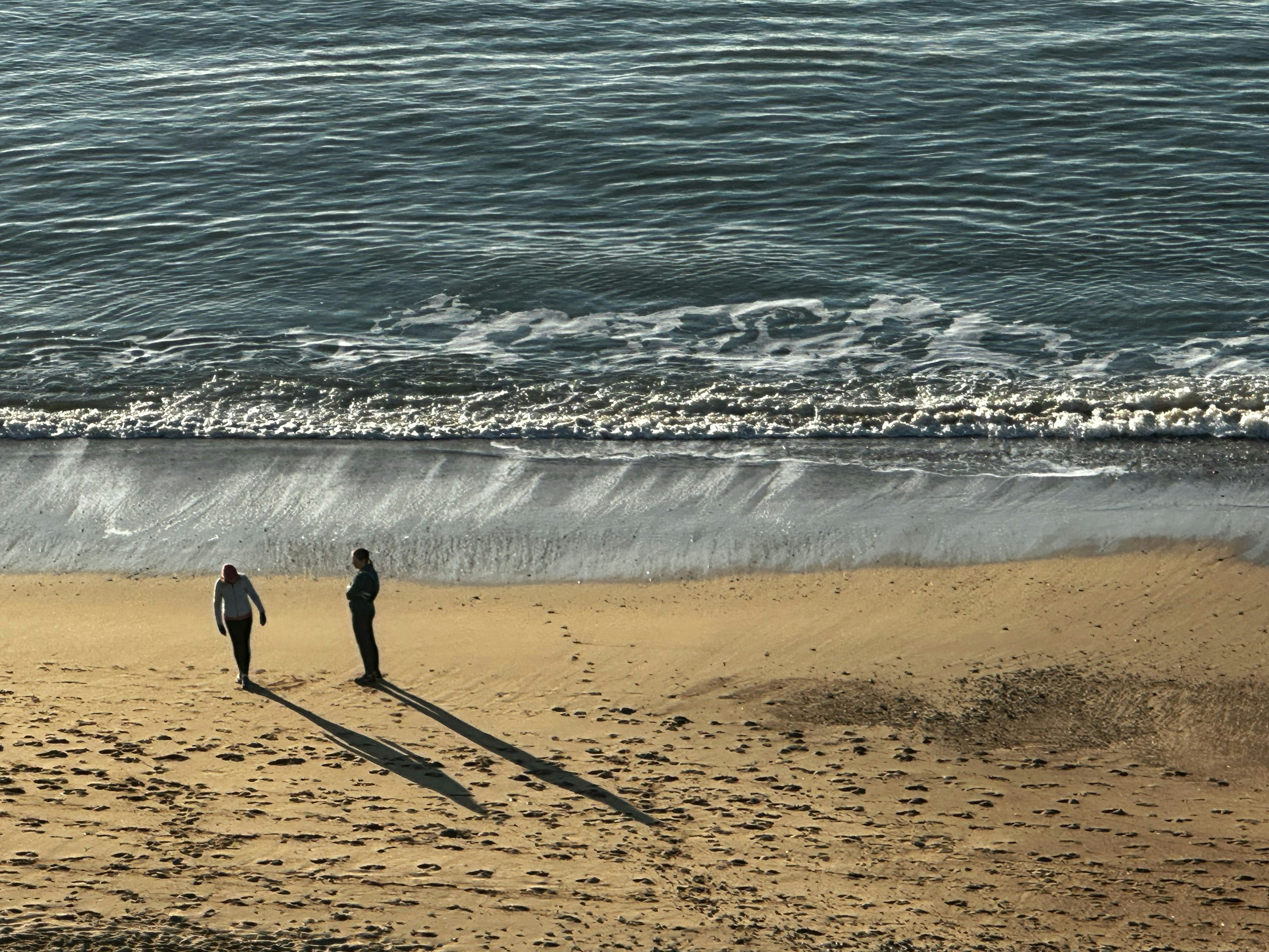 a couple of people standing on top of a sandy beach