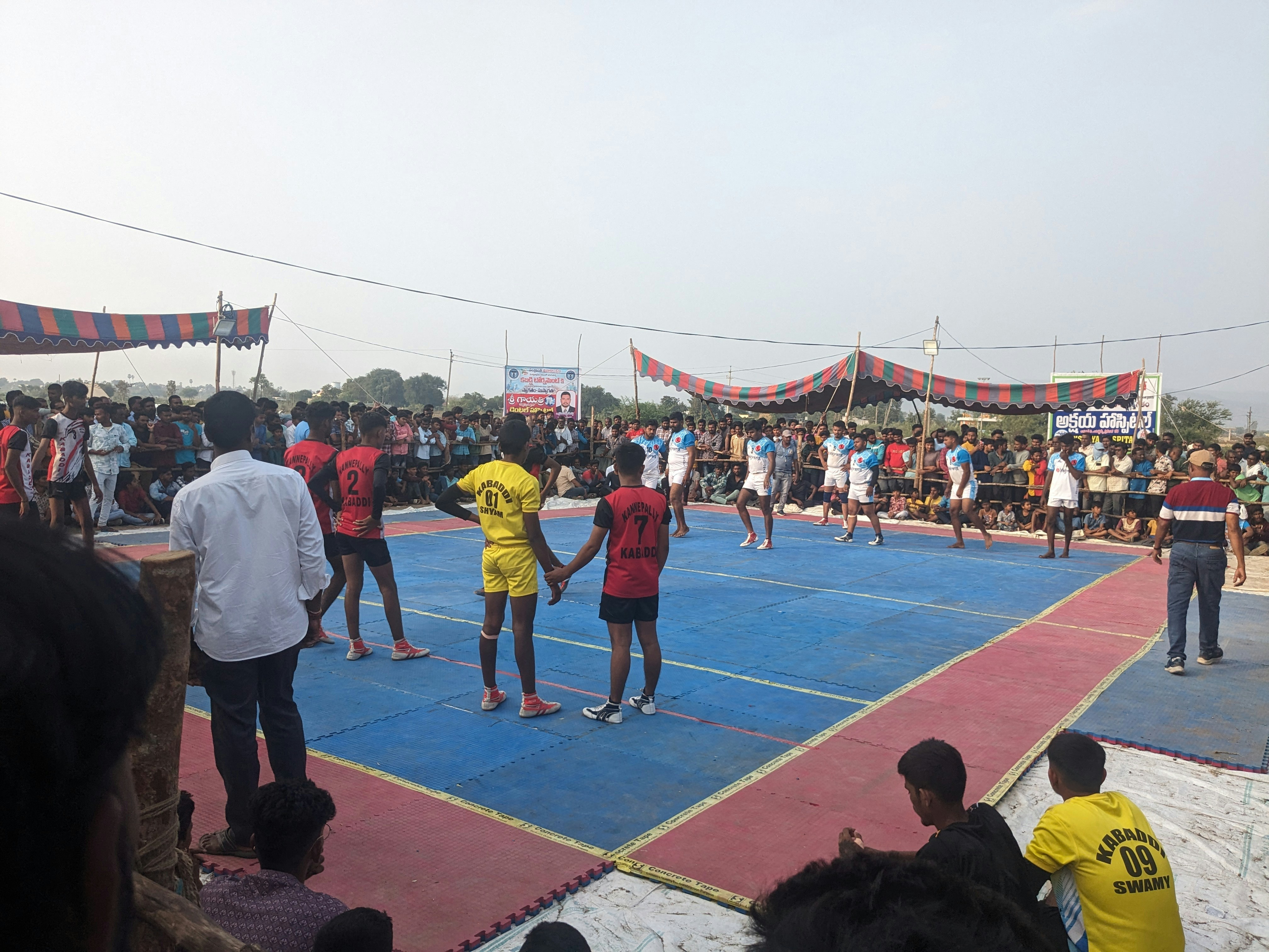 Kabaddi raider mid-tackle on a brightly lit mat with intense crowd energy