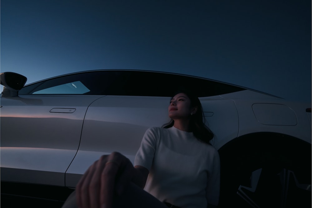 a woman sitting in front of a white car