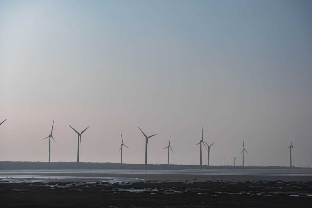 a group of windmills in the distance with a body of water in the fore