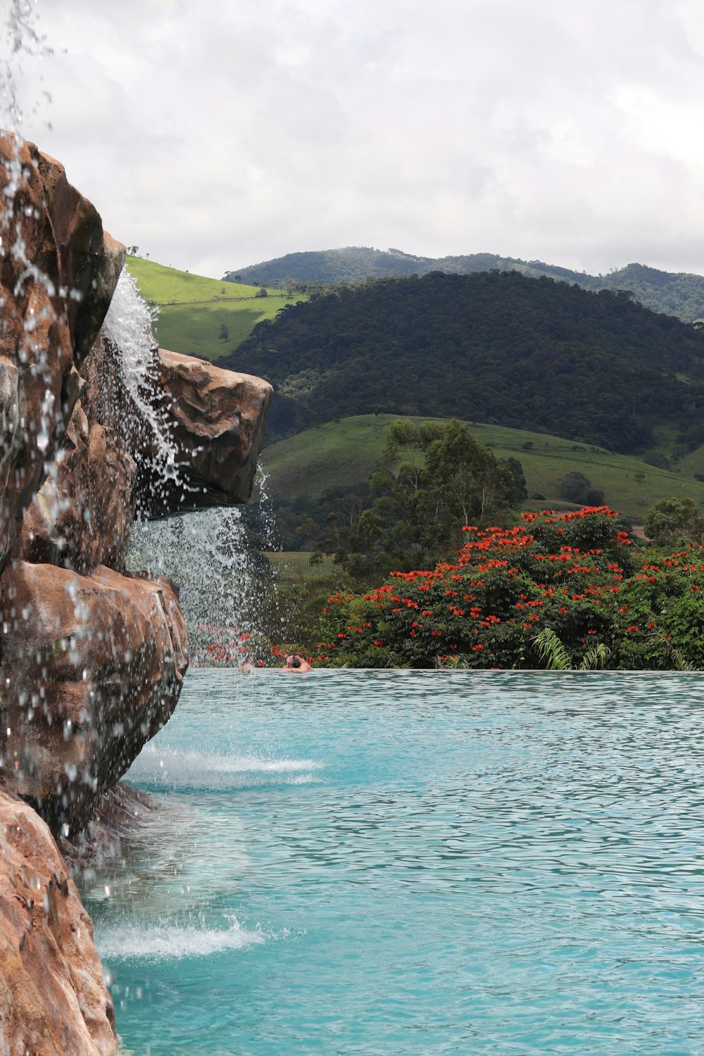 a pool with a waterfall next to a lush green hillside