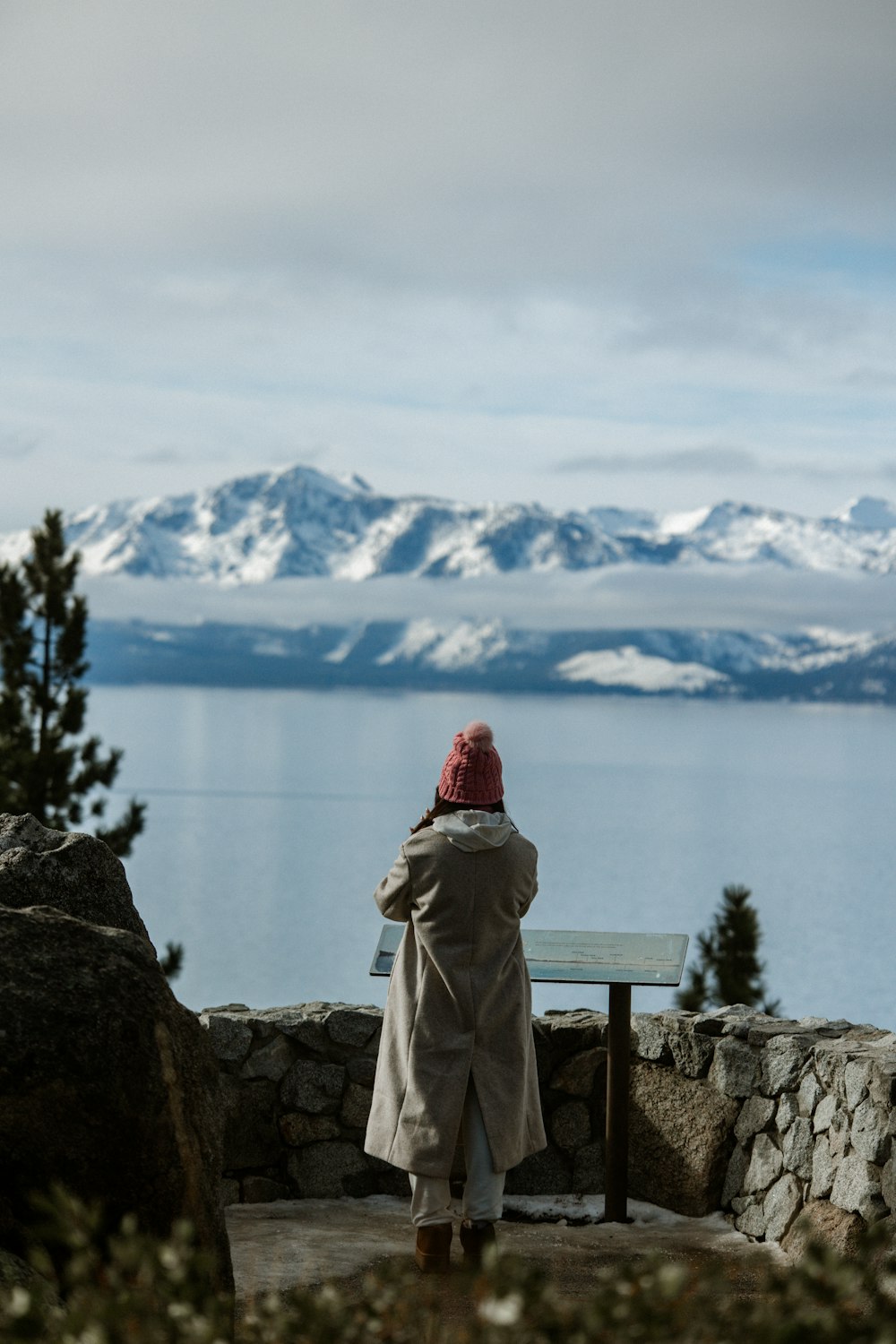 a person wearing a coat and a red hat looking out over a lake