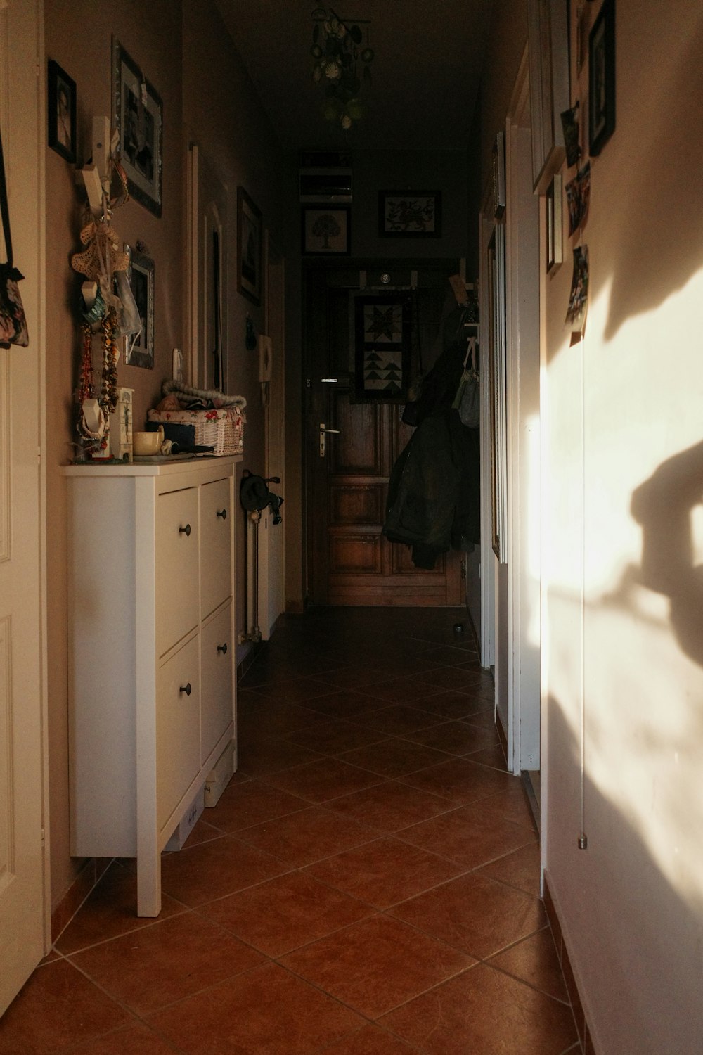 a hallway with a white cabinet and a brown tile floor