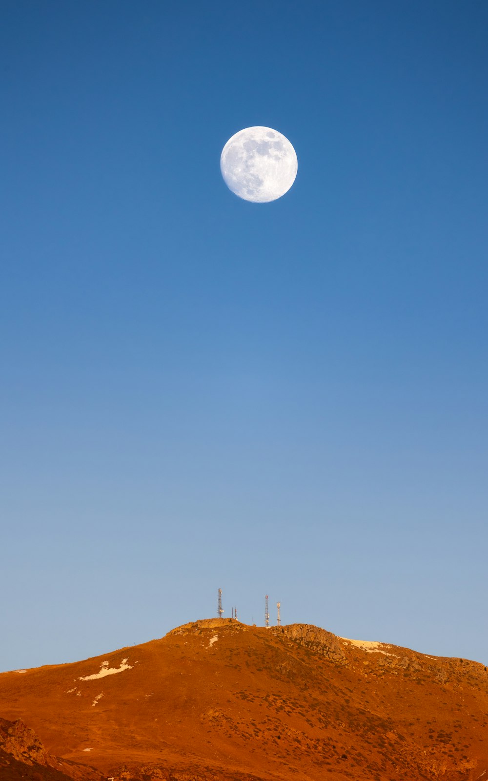 a full moon rising over a hill in the desert