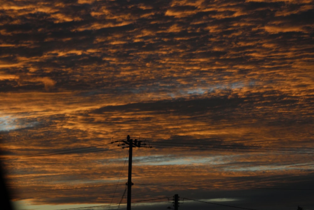 a sunset with clouds and telephone poles in the foreground