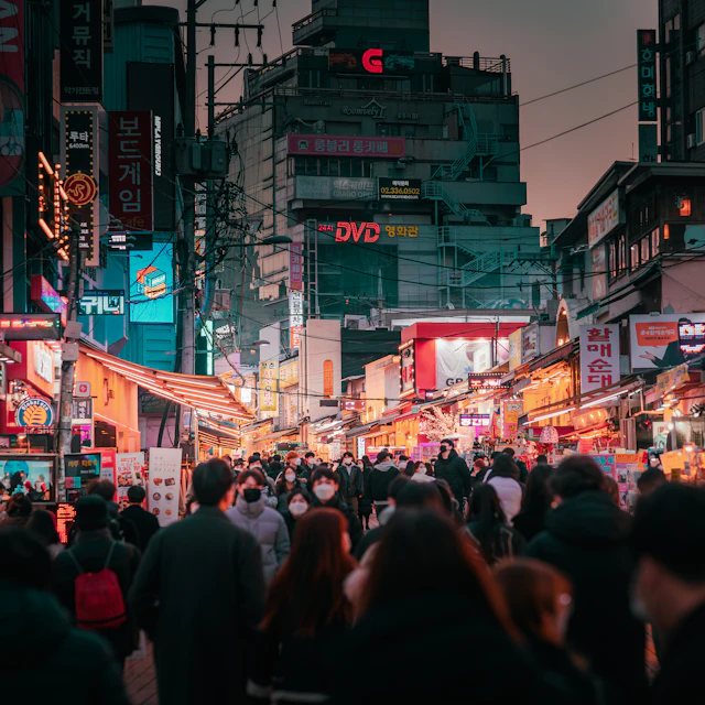 A crowd of people walking down a Seoul street next to tall buildings