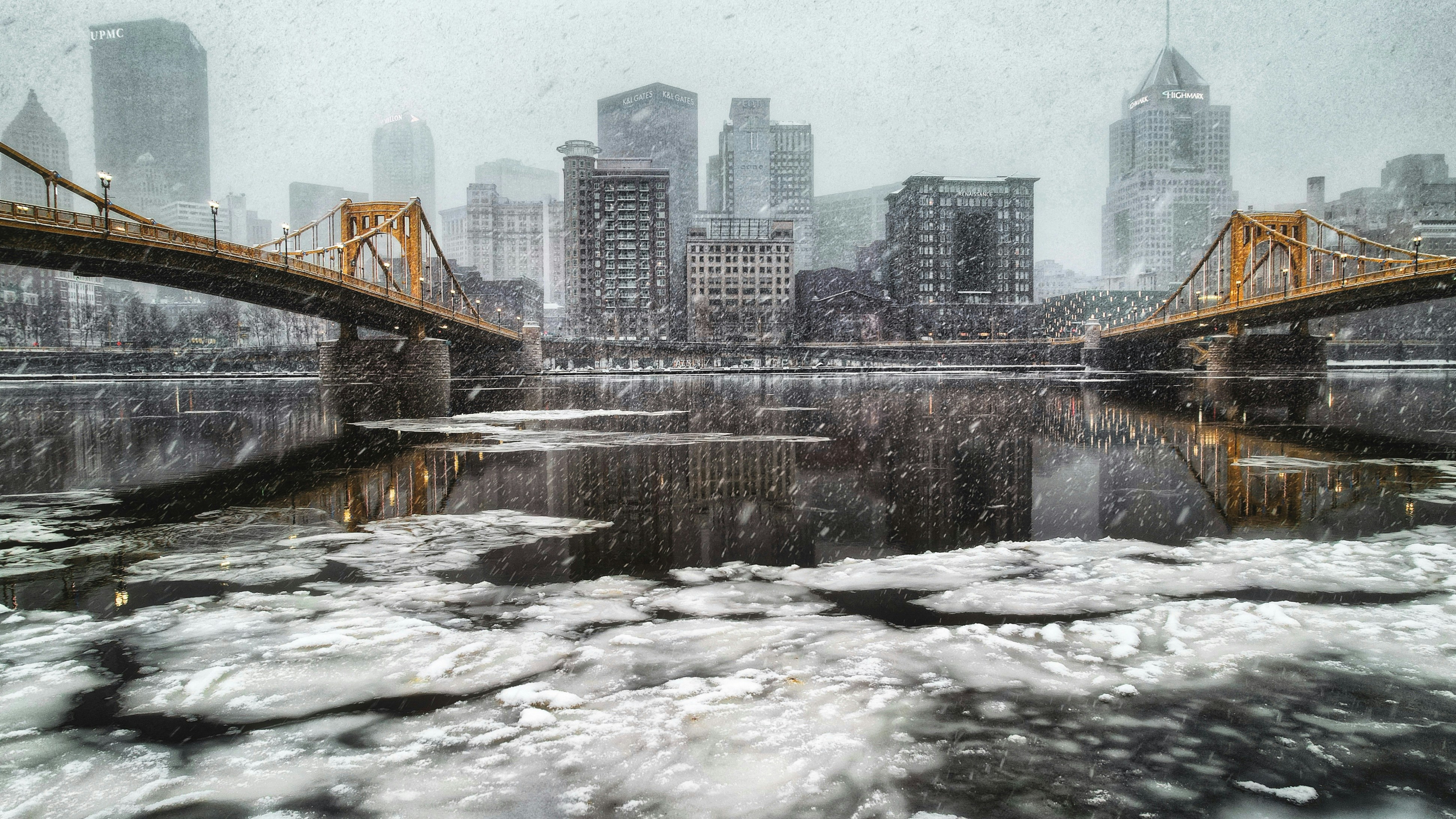 a bridge over a frozen river with a city in the background, Snowy Pittsburgh
