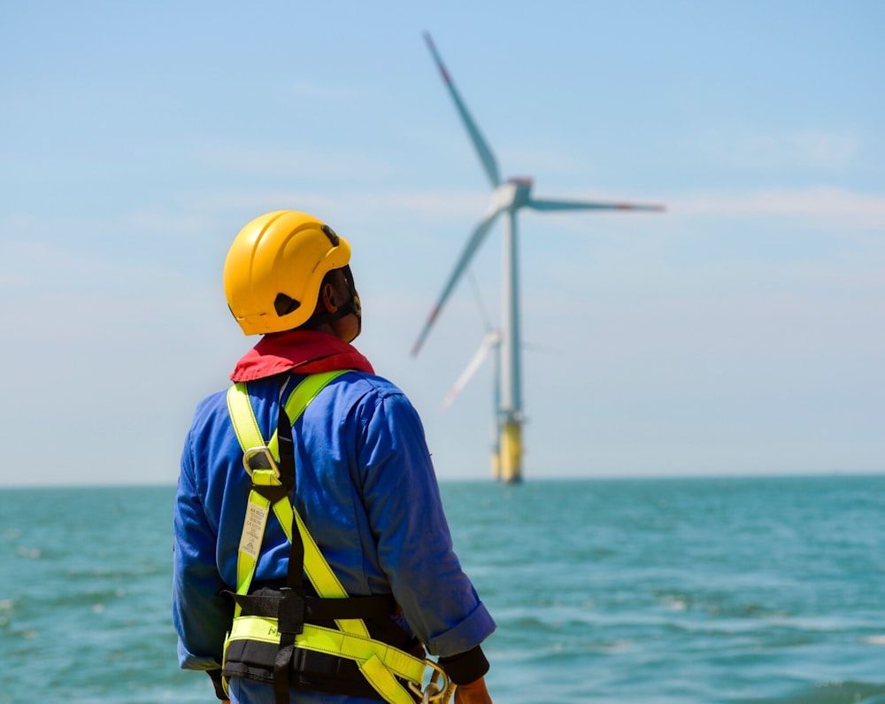 Un uomo con un elmetto e un equipaggiamento di sicurezza che guarda una turbina eolica