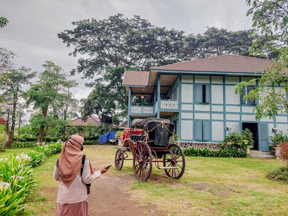 una mujer parada frente a una casa con un carruaje tirado por caballos