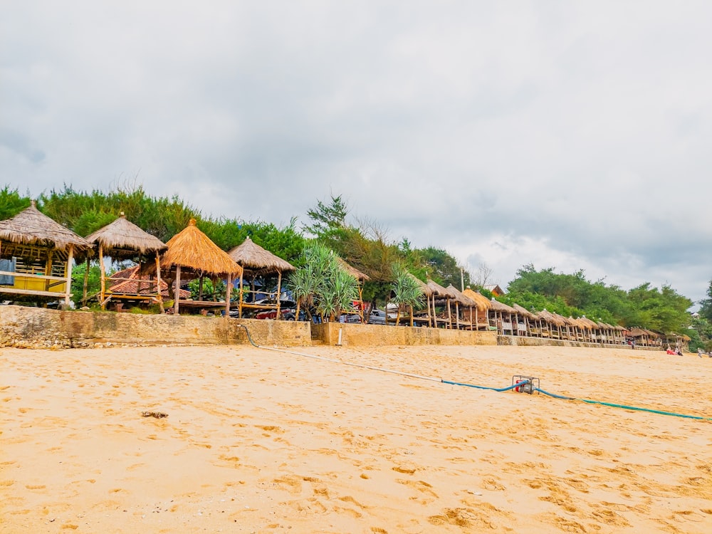 una playa de arena con una hilera de sombrillas con techo de paja