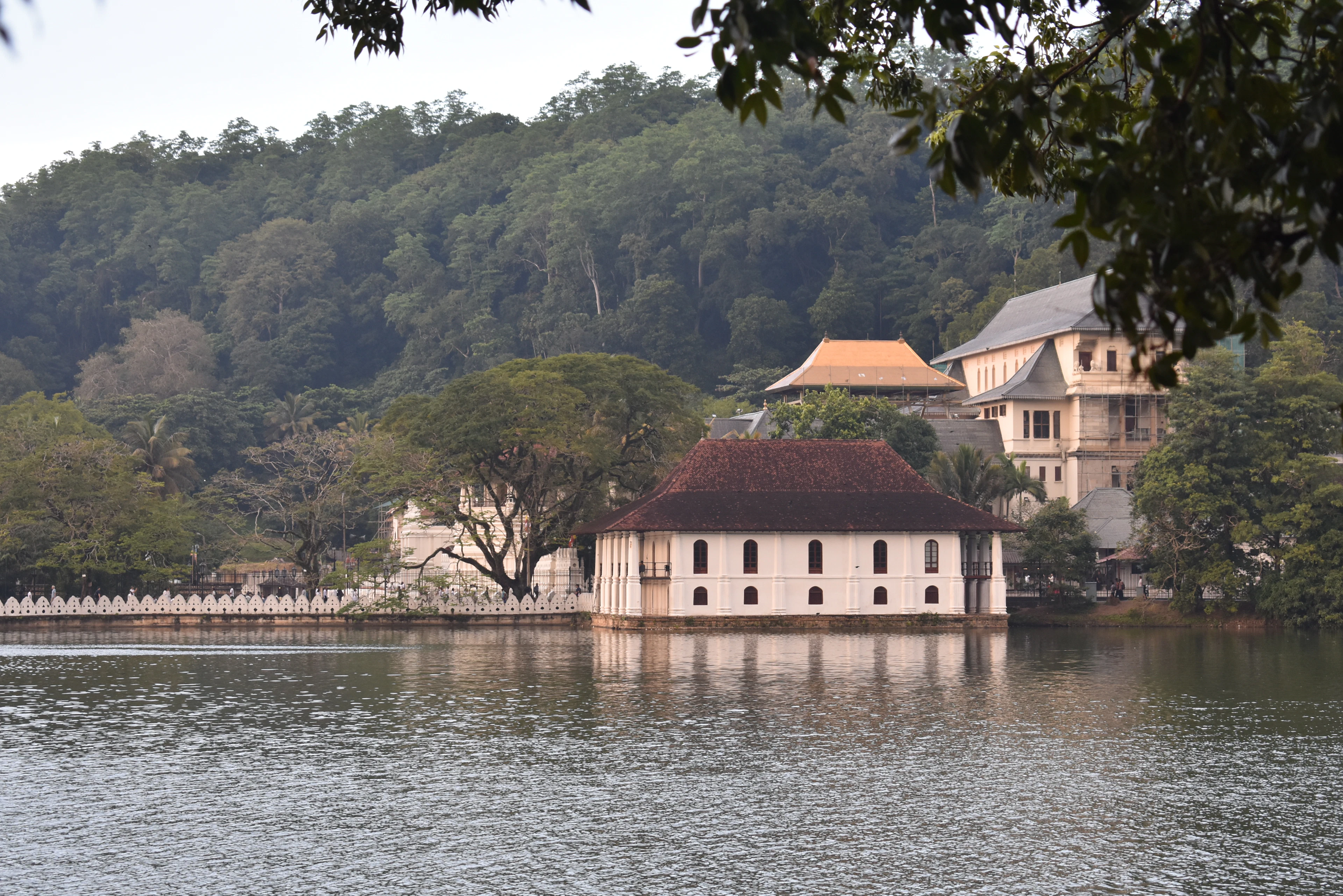 Temple buildings on the shore of Kandy Lake, with forested hills behind