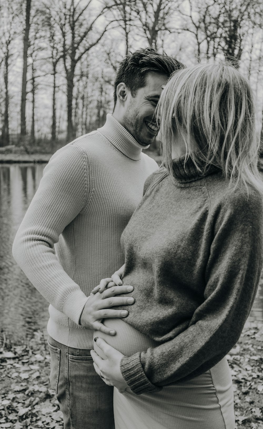 a man and woman standing next to each other in front of a lake