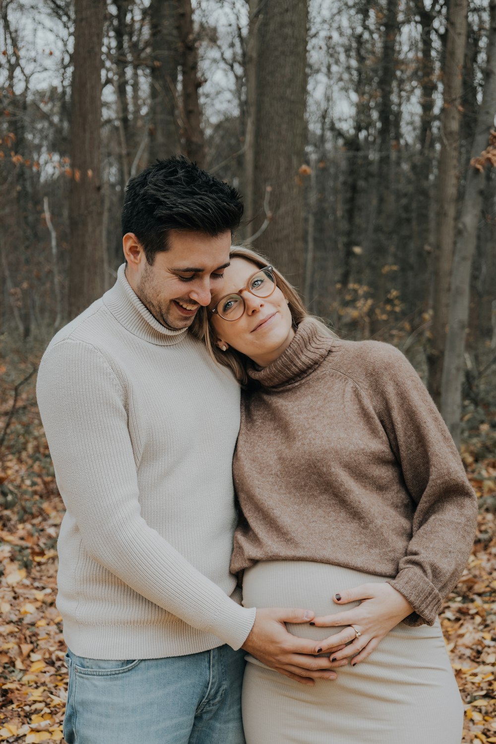 a pregnant couple cuddling in the woods