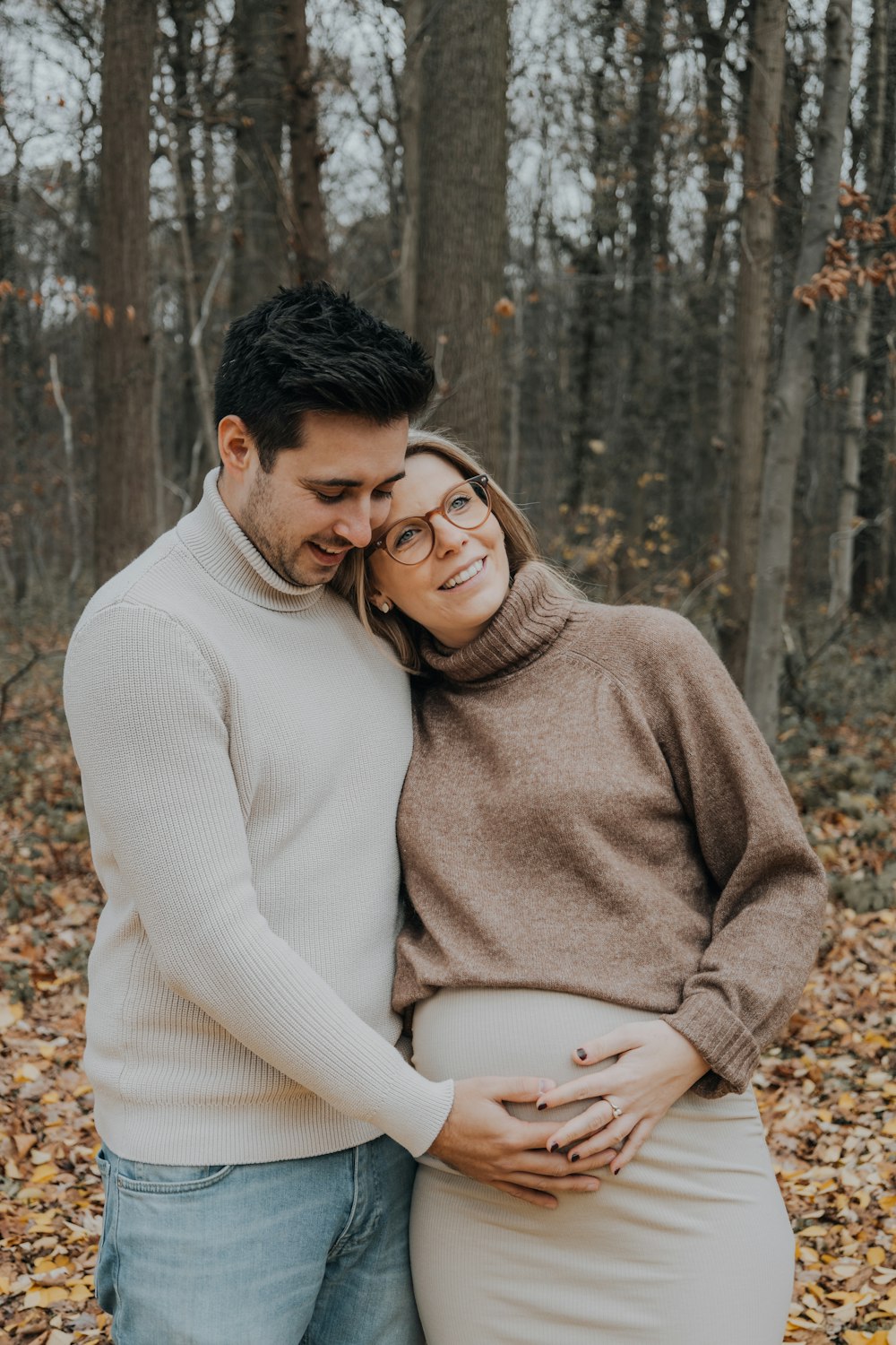 a pregnant couple cuddling in the woods