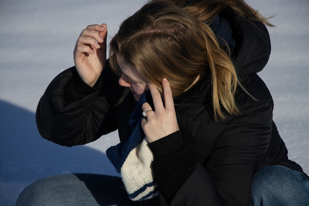 a woman sitting in the snow talking on a cell phone