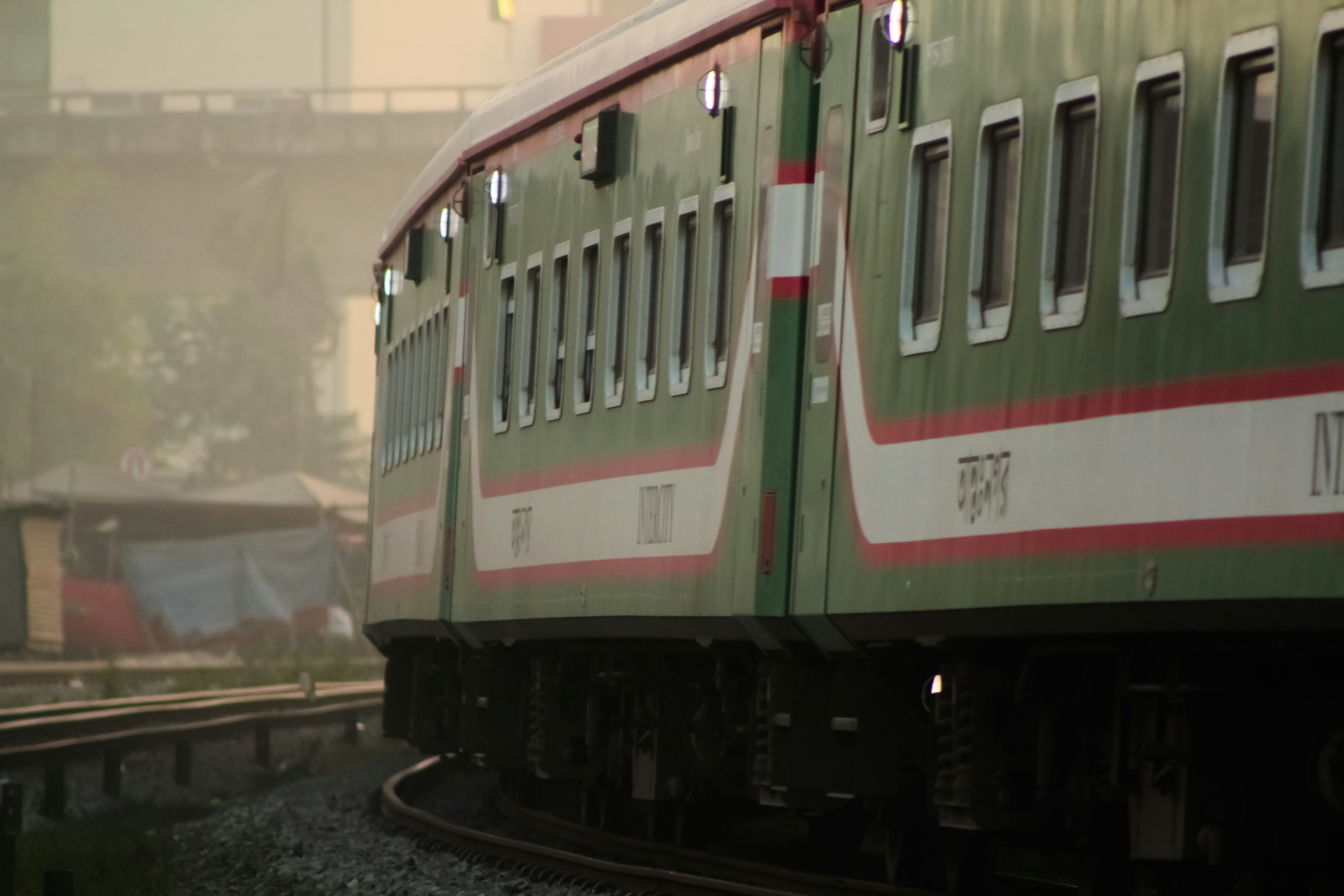 A high-angle shot of a sleek, modern Rajdhani Express train (red and white livery) speeding through a green, scenic landscape, possibly near a small town or station.