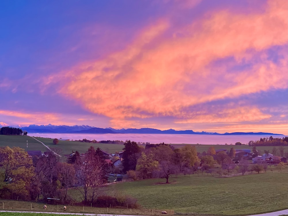 Un beau coucher de soleil sur un champ verdoyant avec des maisons et des montagnes au loin