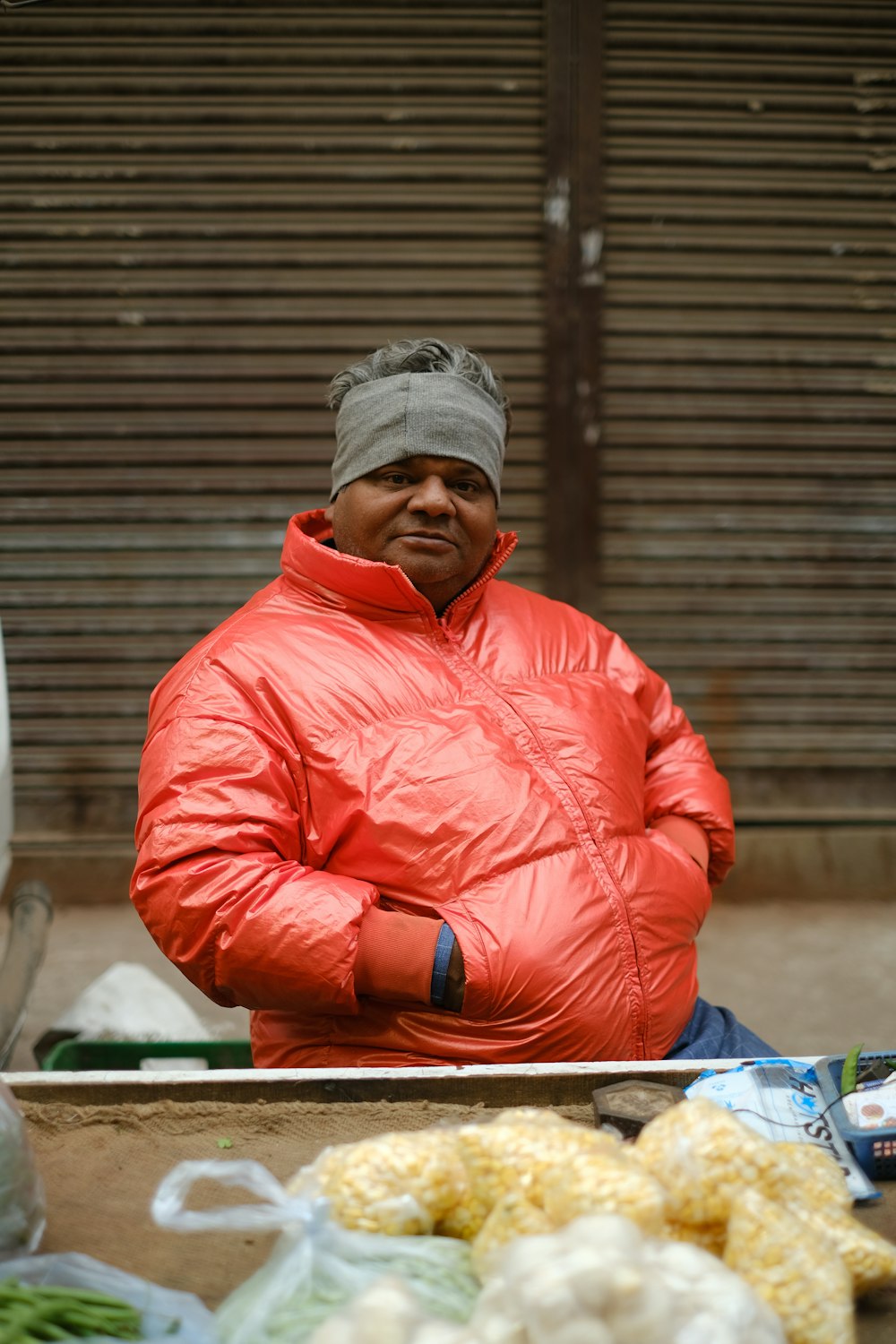 a man in a red jacket standing in front of a table full of vegetables