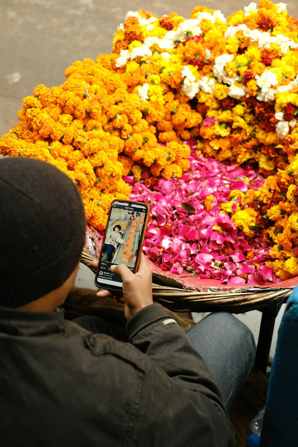 a man sitting in front of a bunch of flowers holding a cell phone