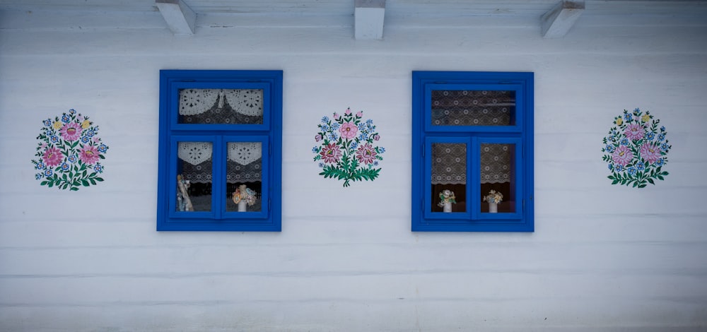 a white wall with blue windows and flowers painted on it