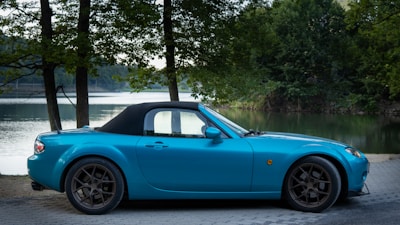 a blue sports car parked next to a lake