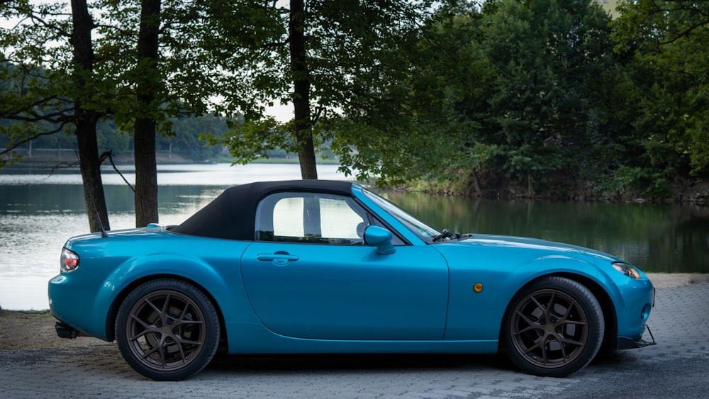 a blue sports car parked next to a lake