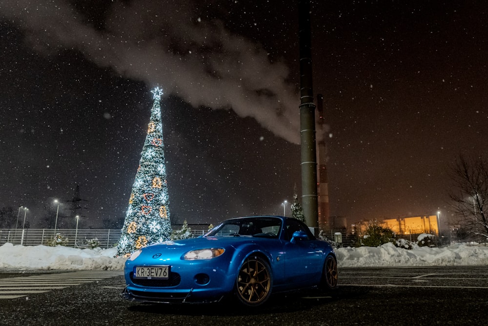 Um carro esportivo azul estacionado em frente a uma árvore de Natal