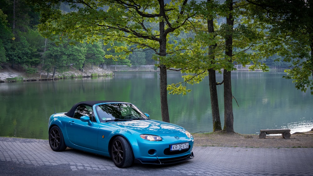 a blue sports car parked next to a lake