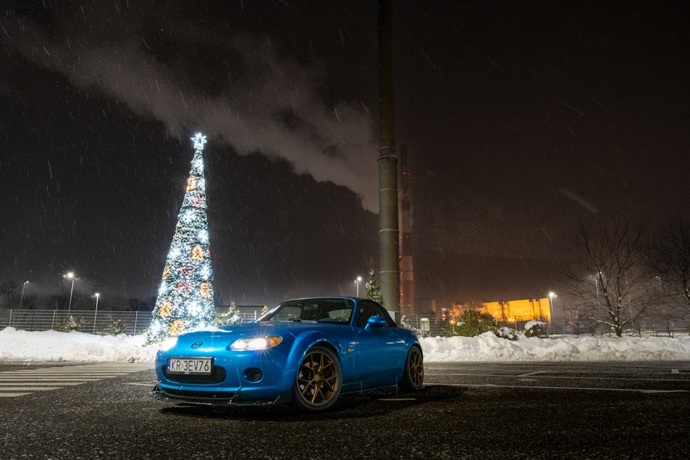 Une voiture de sport bleue garée devant un sapin de Noël