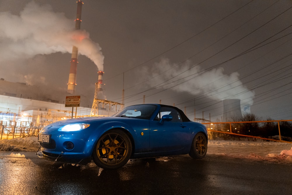 um carro esportivo azul estacionado em frente a uma fábrica