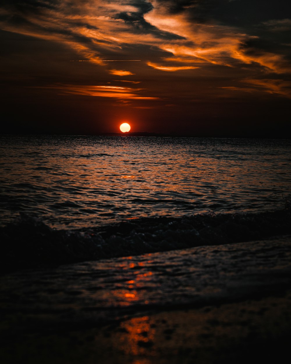 the sun is setting over the ocean on a cloudy day