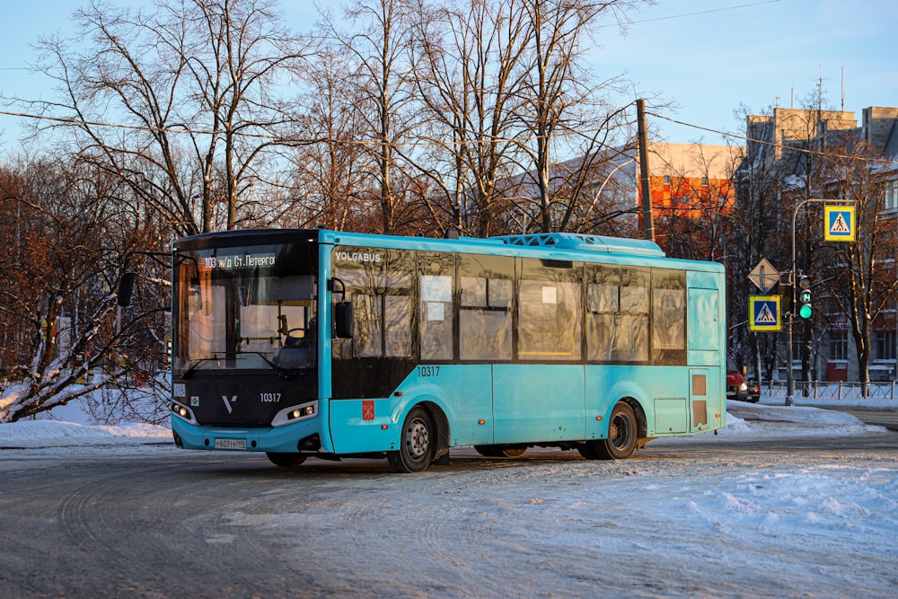a blue bus driving down a snow covered road