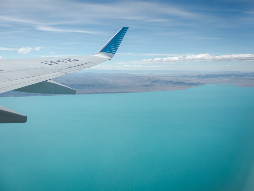 el ala de un avión volando sobre un cuerpo de agua