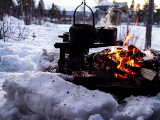 a campfire with a kettle on top of it in the snow