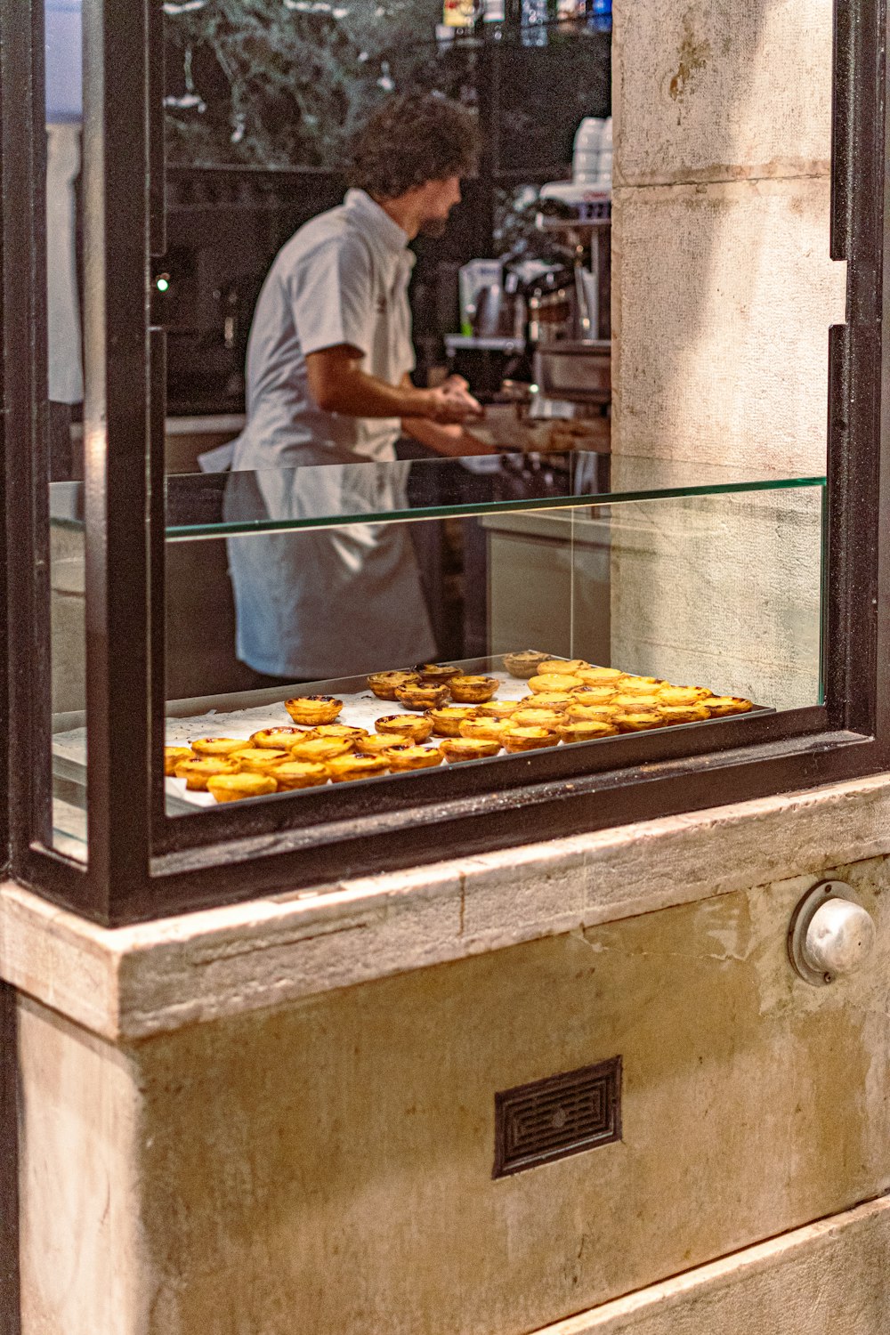 Un hombre preparando comida detrás de un mostrador de cristal
