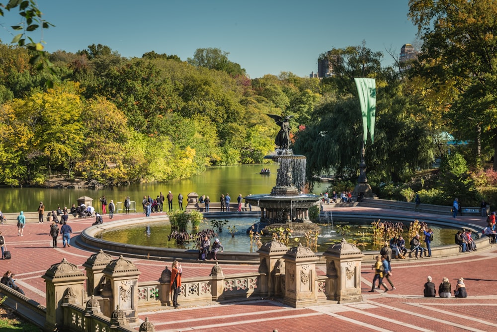 a group of people standing around a fountain in a park