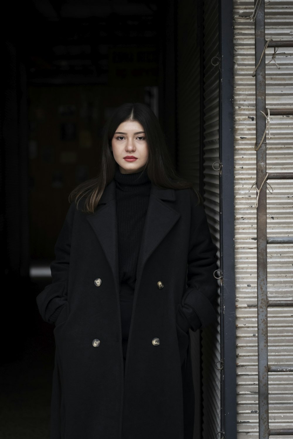 a woman standing in front of a door wearing a black coat