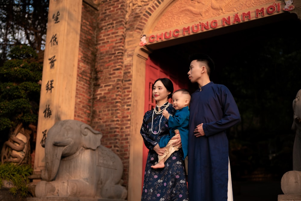 a man and woman holding a baby in front of a building