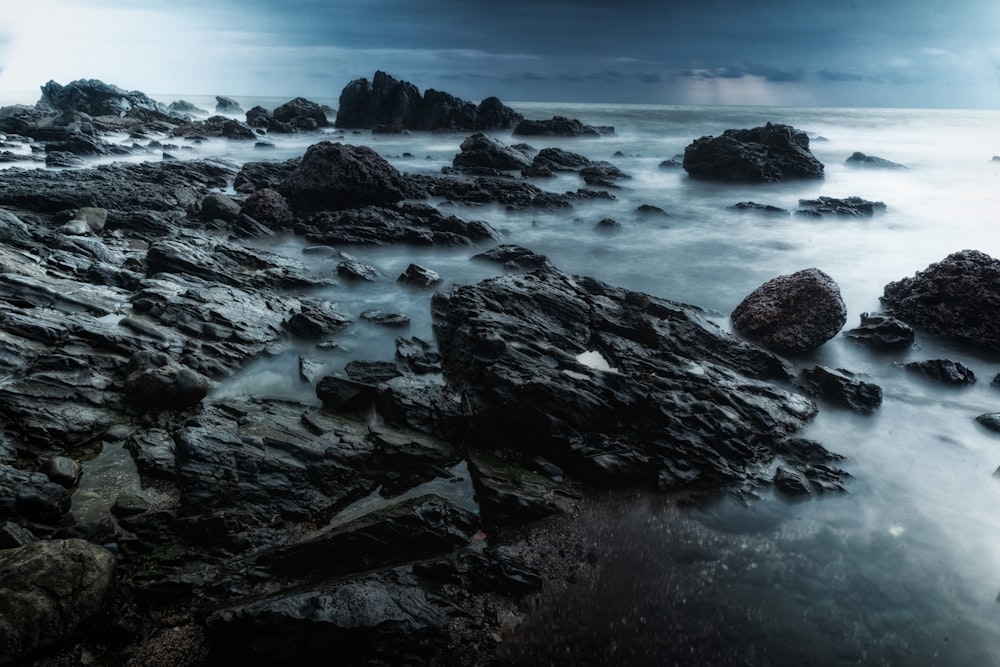 a beach with rocks and water under a cloudy sky