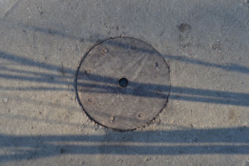 a manhole cover on the ground with a shadow of a person