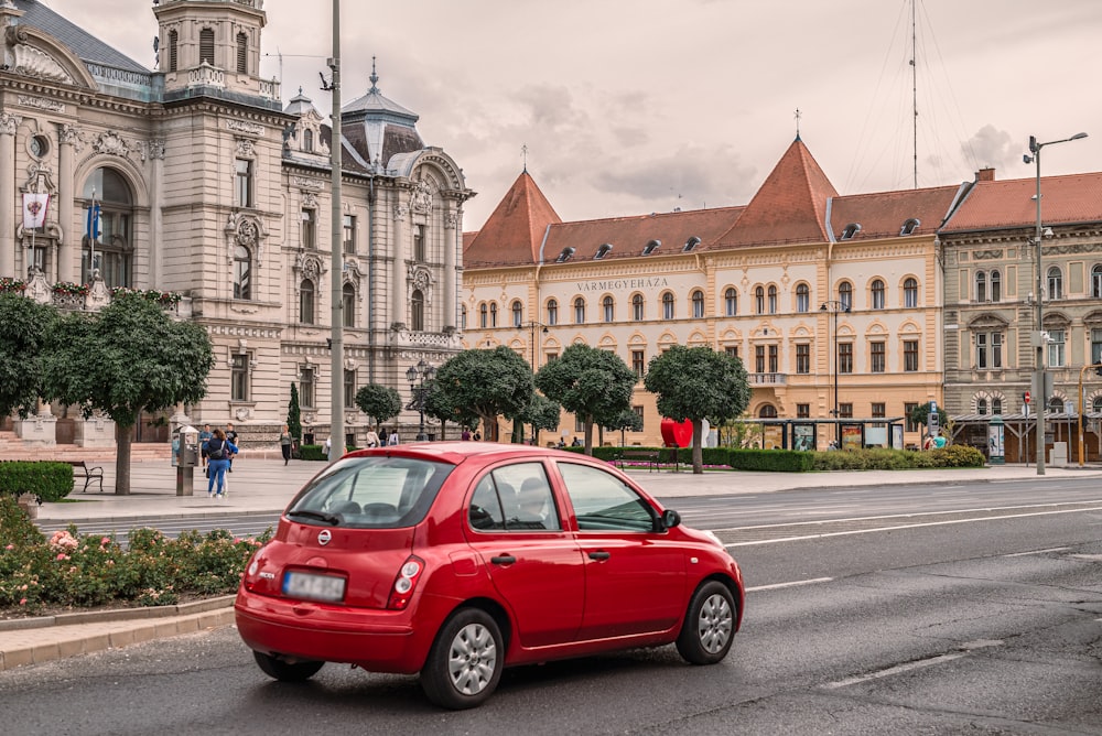 a red car driving down a street next to tall buildings