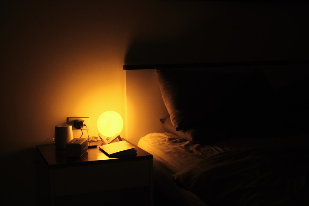 a night stand with a lamp on it next to a bed