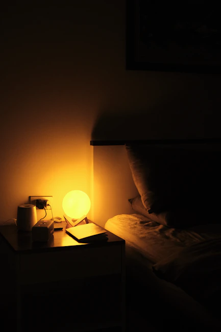 Bedside lamp beside a closed notebook in a calm bedroom at night