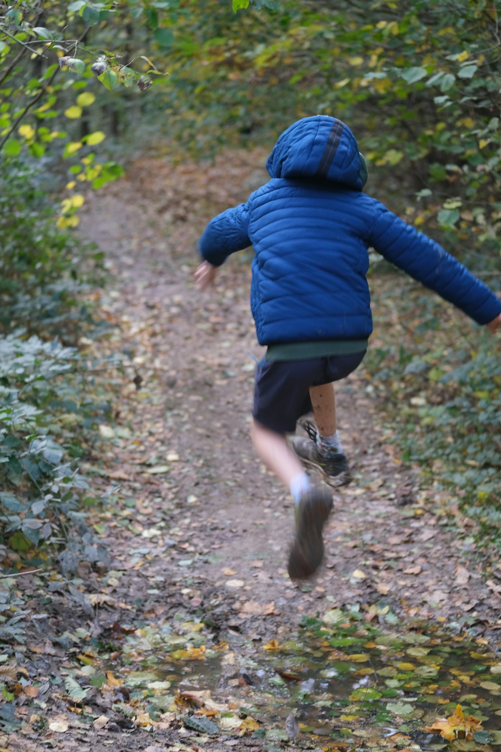 a young boy is running down a path in the woods