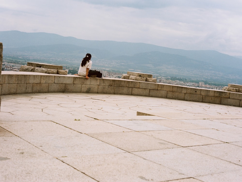 a woman sitting on top of a stone wall
