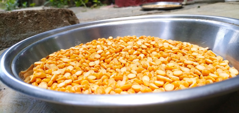 a metal bowl filled with corn kernels on top of a table